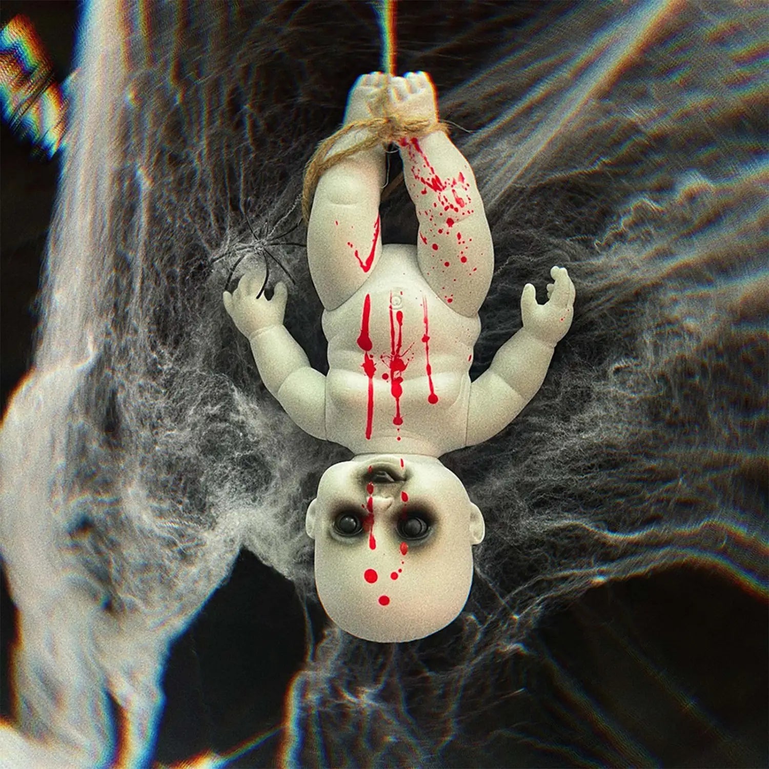 A white plastic Halloween hanging ghost doll with red paint splatters hanging upside down by a string as a spooky prop.