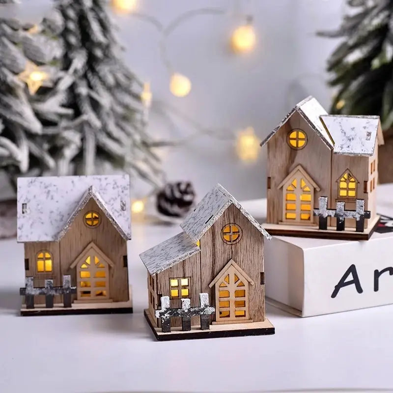 Drei Miniatur-Holz-Weihnachtshäuser mit schneebestäubten Dächern und leuchtend gelben Fenstern, die mit LED-Lichtern erhellt werden, als leuchtende Weihnachtsdekoration.