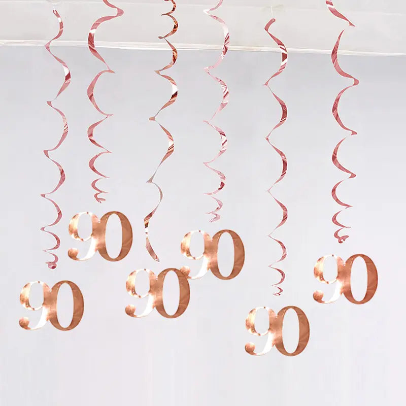 Décorations en tourbillon d’anniversaire doré rosé avec des guirlandes en spirale métalliques et des découpes suspendues du numéro 90.