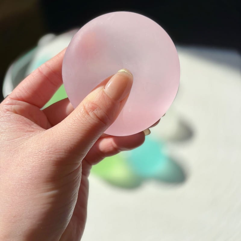 A translucent pink circular blue mochi squeeze sensory fidget toy held in a hand.