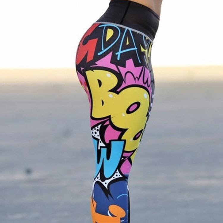 Vibrant graffiti workout leggings with a high waist black elastic waistband featuring bold yellow pink blue and red comic book lettering in pop art style.