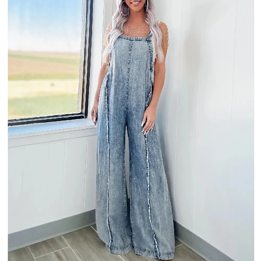 women wide leg denim jumpsuit featuring light-wash denim material with frayed side seams and a square neckline in a vintage long overall style.