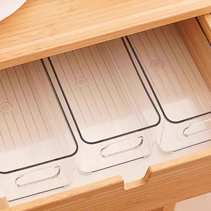 Bacs de rangement pour réfrigérateur en plastique transparent, avec bordure noire et poignées intégrées, disposés avec soin dans un tiroir en bois.