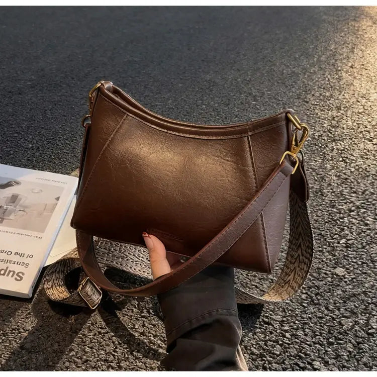 柄のあるストラップとゴールドトーンの金具を備えた、女性用ブラウンレザーのクロスボディショルダーバッグ。