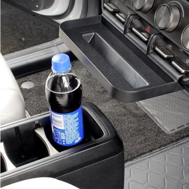 una botella de refresco de plástico azul con una tapa azul a juego colocada en el portavasos de la bandeja organizadora para consola central Icar V23 en el interior de un automóvil