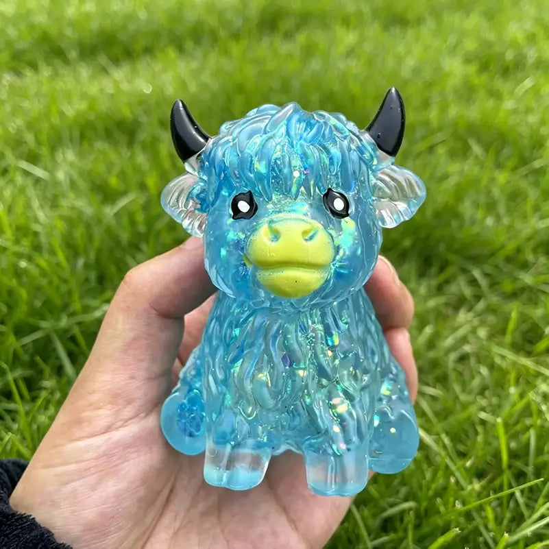 A translucent blue glittery plastic highland cow sensory fidget toy with black horns and a yellow snout designed for stress relief.