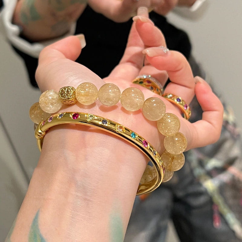 Ein Armreifarmband aus goldfarbenem Multigemsteinschmuck mit aufwendigen Details und lebhaft farbigen Steinen auf poliertem Goldmaterial.