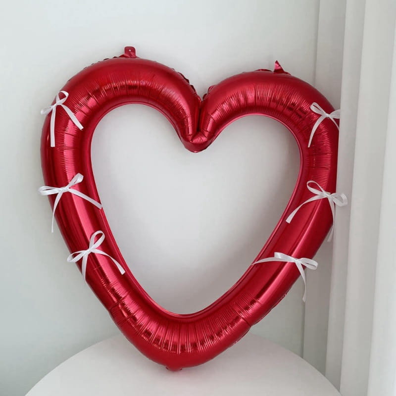 Un globo de lámina con corazón rojo brillante para marco de foto de 40 pulgadas, adornado con cintas blancas atadas alrededor de sus bordes.