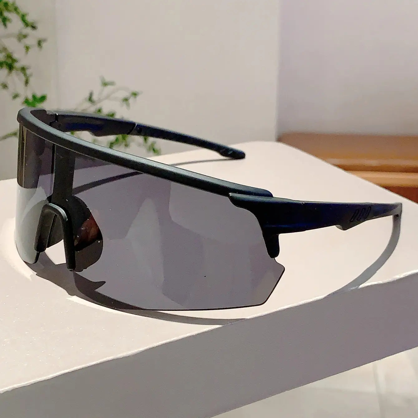 Lunettes de soleil de sport surdimensionnées à monture noire, verres réfléchissants gris foncé et design aérodynamique élégant pour le cyclisme.