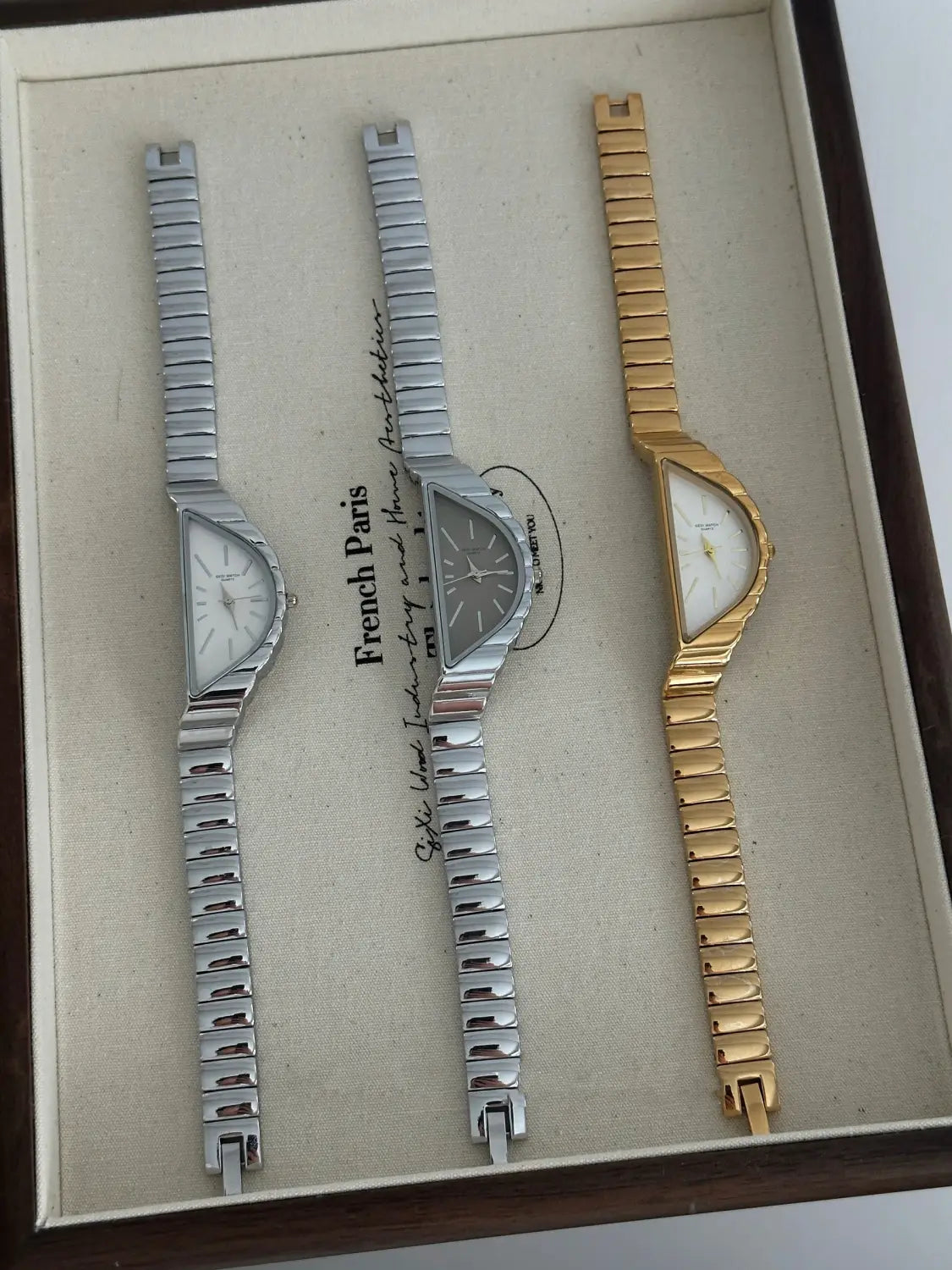 Three elegant geometric triangle quartz watches with metallic link bracelets in silver and gold-tone stainless steel finishes.