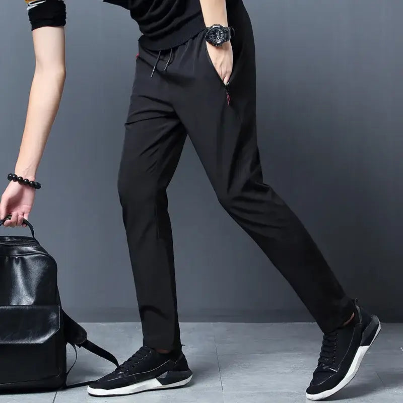 Joggers casuales ajustados para hombre en tejido deportivo negro, con cintura con cordón y pespuntes de acento rojo sutiles.