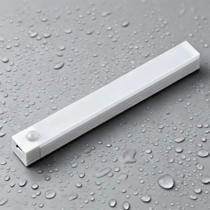 Lámpara lineal LED rectangular blanca con bordes redondeados, que presenta un diseño moderno y refinado e incluye un sensor de movimiento visible desde el ángulo frontal.