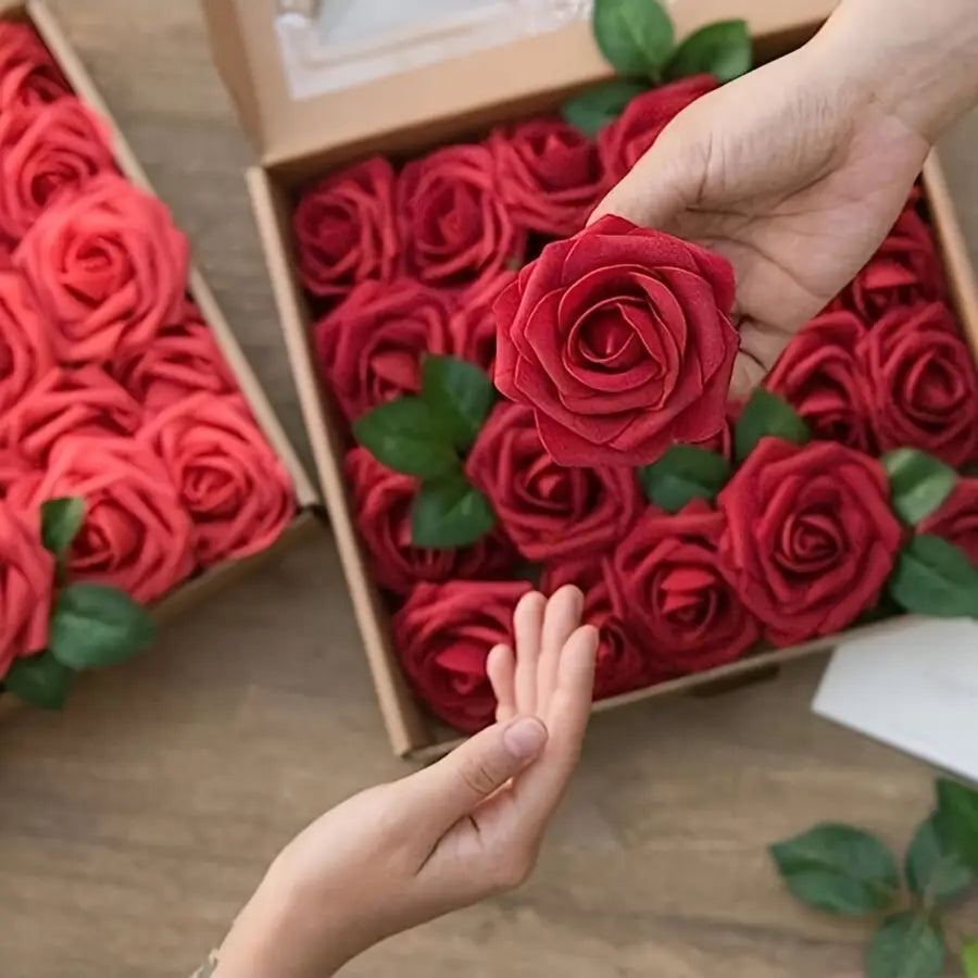 Une main tient délicatement une rose en savon de fleurs artificielles rouges vibrantes, aux pétales superposés avec minutie et aux feuilles vertes réalistes, pour la décoration.