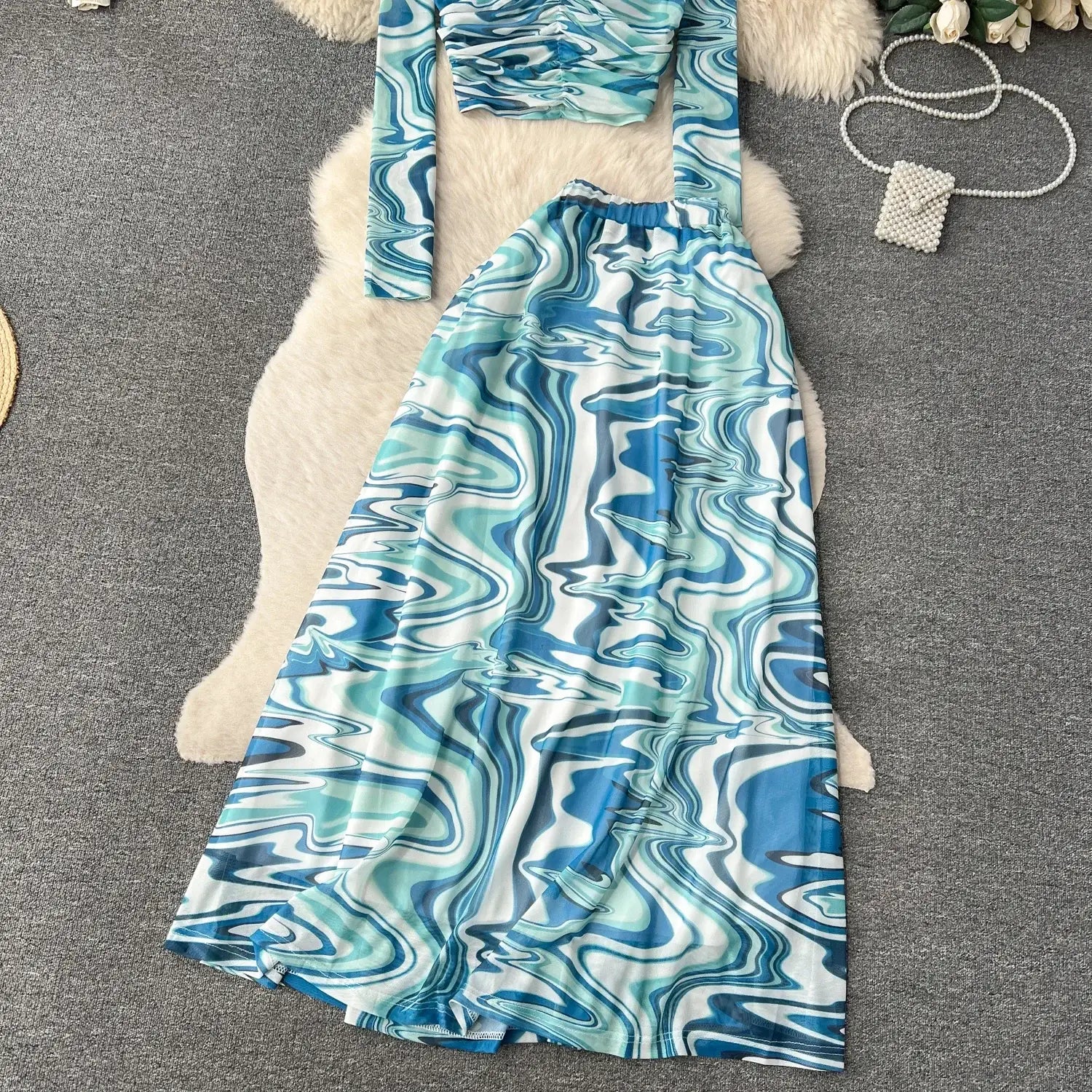 A flowing two-piece mesh skirt set with a long-sleeved top and matching maxi skirt featuring an abstract blue and white marbled print and an elastic closure type.