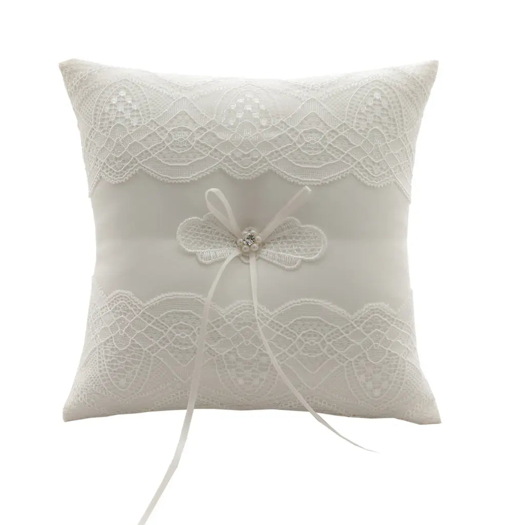 Almohada blanca para anillos de boda de encaje con delicado bordado floral y lazo central, con una piedra preciosa brillante, diseñada como almohadilla portadora de arras.