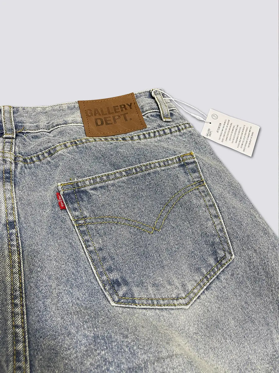 Die Rückseite der hell gewaschenen Patchwork-Denim-Glockenjeans aus Denim mit einem braunen Lederpatch, das mit Gallery-Dept geprägt ist, sowie einem roten, eingenähten Steg in der Rückentasche.