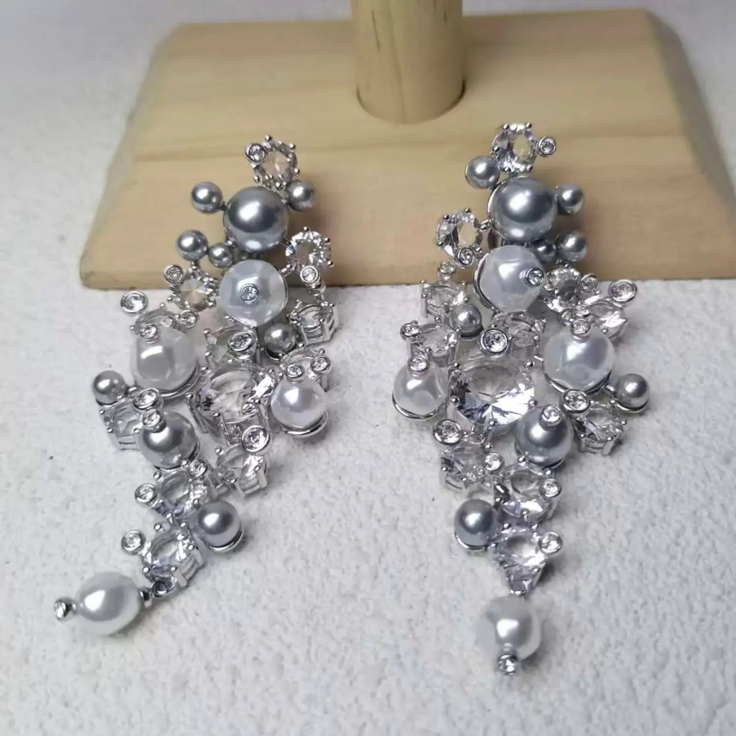 Pendientes tipo candelabro en tono plateado y con cristales transparentes, adornados con perlas y pedrería en capas, del conjunto de joyería de cristal que incluye un collar de plata, pendientes y una pulsera.