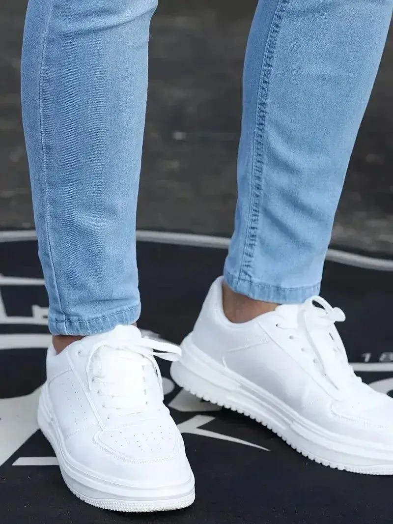 Baskets à plateforme blanches avec un design minimaliste et épuré, rehaussées de détails perforés, associées à des jeans en denim bleu foncé coupe slim pour homme.