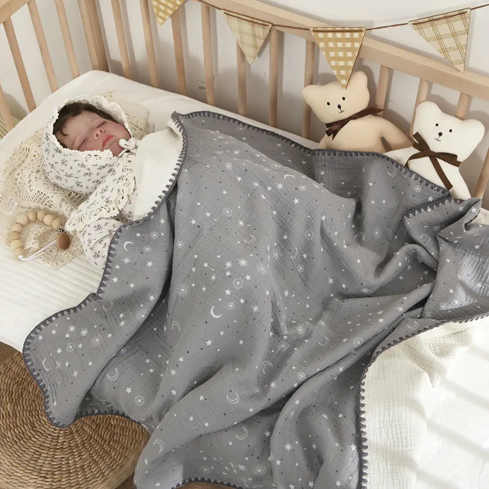 やわらかな通気性のある質感を特徴とする、グレーの星と月の模様のムスリンコットンのベビースワドルブランケット。