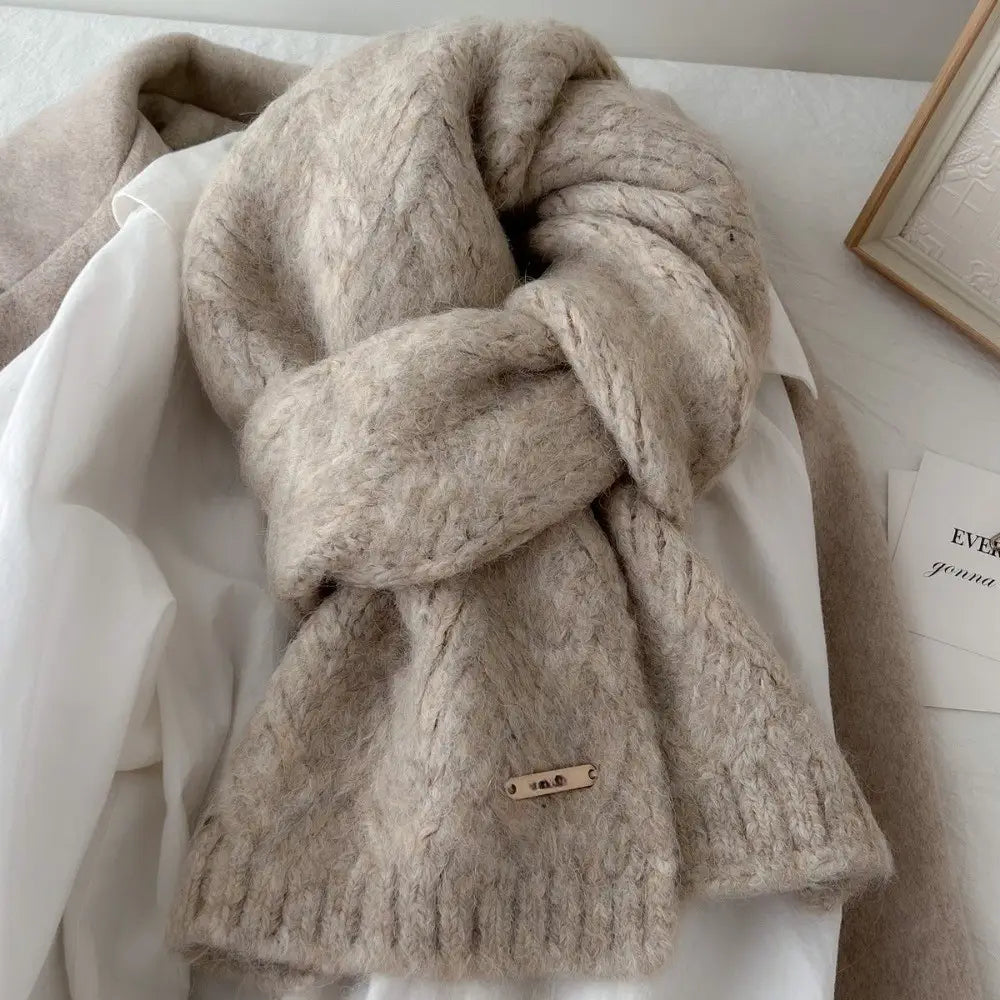 Una bufanda de punto de invierno para mujer color beige, con un patrón de trenzado con textura y una pequeña etiqueta metálica, diseñada como chal calentador de cuello cálido.