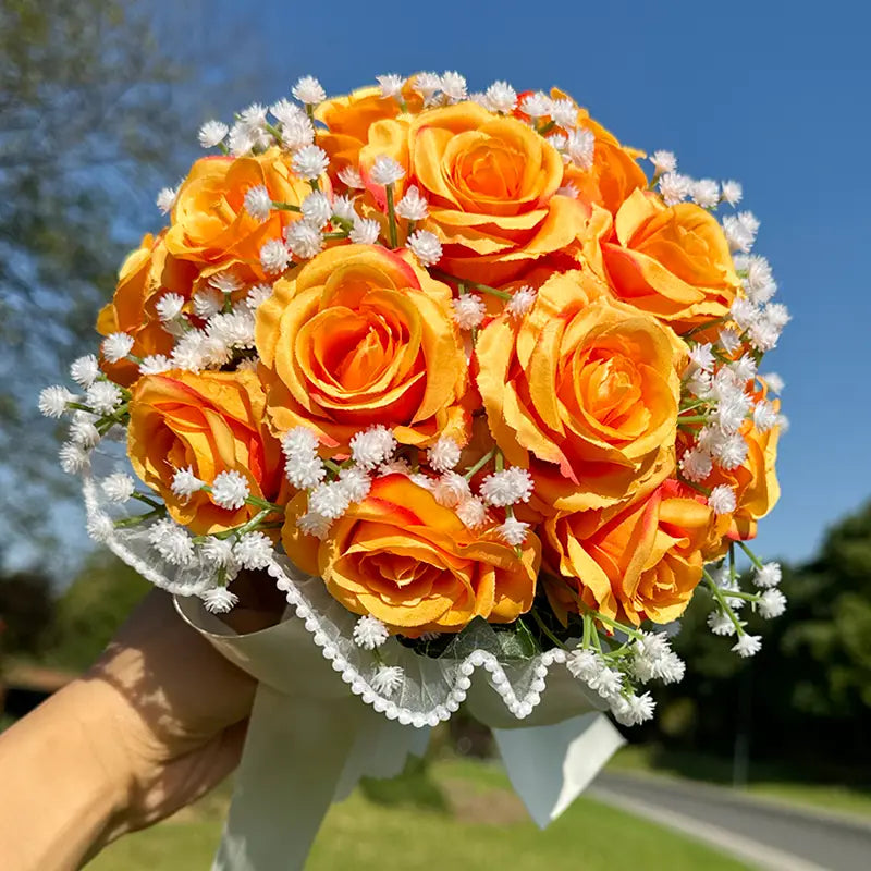 A vibrant white silk rose wedding bouquet featuring artificial orange roses accented with delicate white babys breath and tied with a sheer lace ribbon.