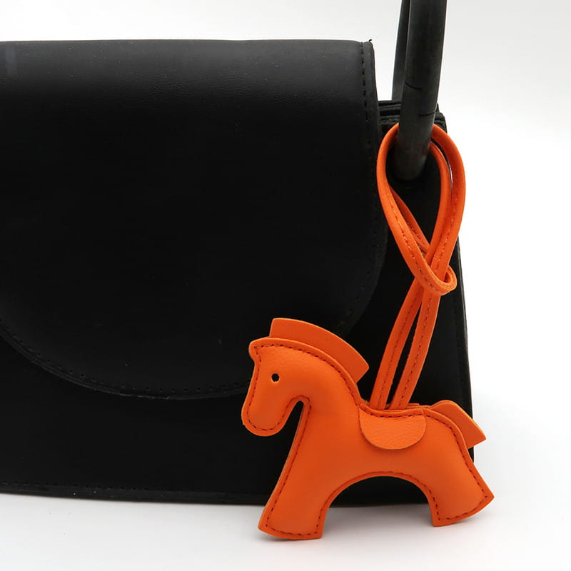 Porte-clés en cuir orange en forme de cheval avec lanière bouclée, fixée à une anse noire.