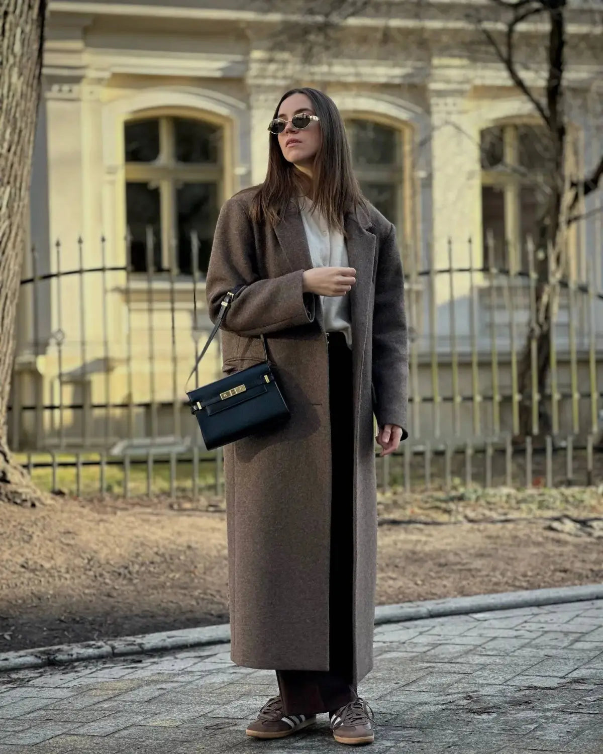 A navy blue leather kelly bag with gold hardware paired with a brown wool blend overcoat for women winter commuter jacket.