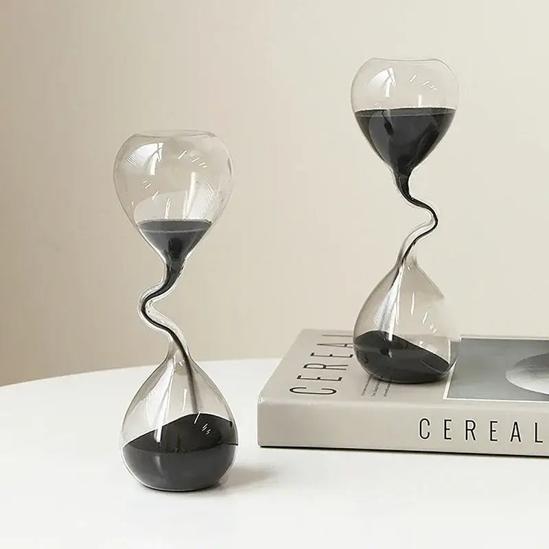 Two transparent glass hourglass timers with black sand and a distinctive twisted neck design ideal for home decoration.