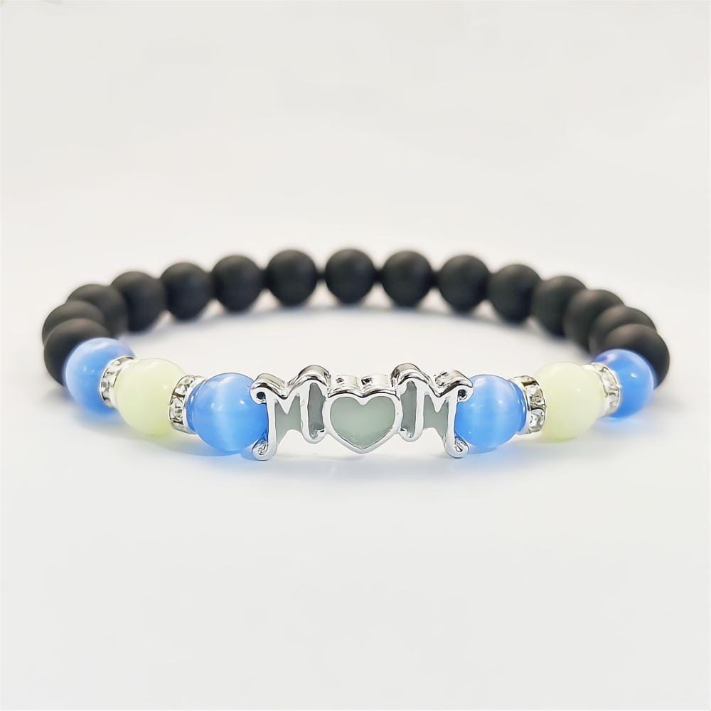 Brazalete para mamá de color plateado con diseño de corazón, con cuentas negras y azules y pedrería transparente; brilla en la oscuridad, un regalo pensado para mamá.