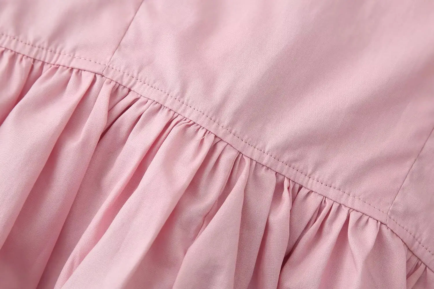 A soft pink slim-fit design dress with a round neckline featuring a gathered ruffled hemline and neat stitching along the seam.