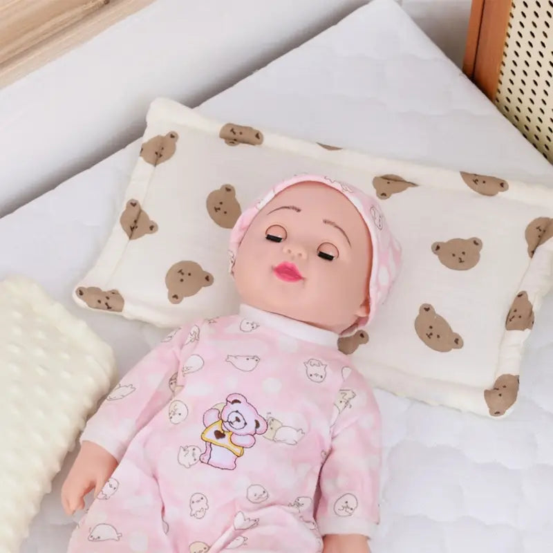 ピンクの赤ちゃん人形が、お揃いのピンク色のコットン製ロンパースを着ており、カートゥーンの動物柄とコーディネートしたピンクの帽子をかぶった状態で、通気性のある乳児の睡眠サポート用コットン枕の上に横たわっています。