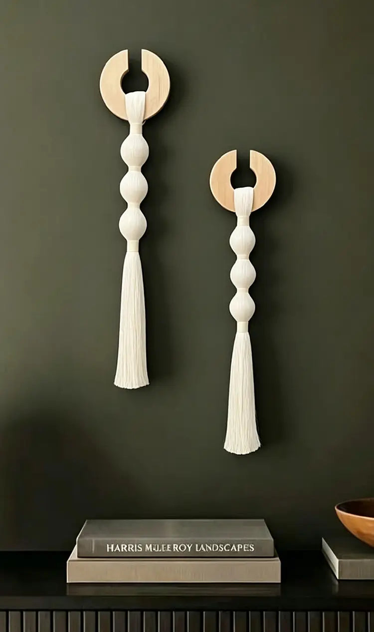 Arte de colgante mural minimalista con borlas tejidas, que presenta un diseño de macramé blanco con una tapa circular de madera y acentos de borlas.