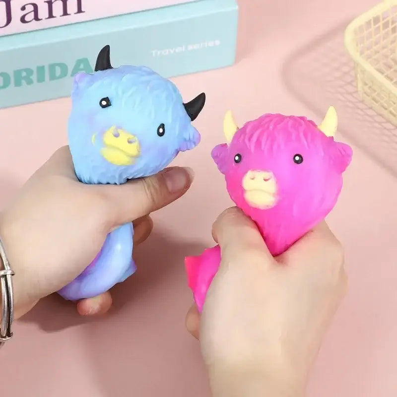 Jouets antistress en forme de vache highland kawaii en matière pelucheuse, comprenant un taureau bleu aux cornes noires et un taureau rose aux cornes jaunes.