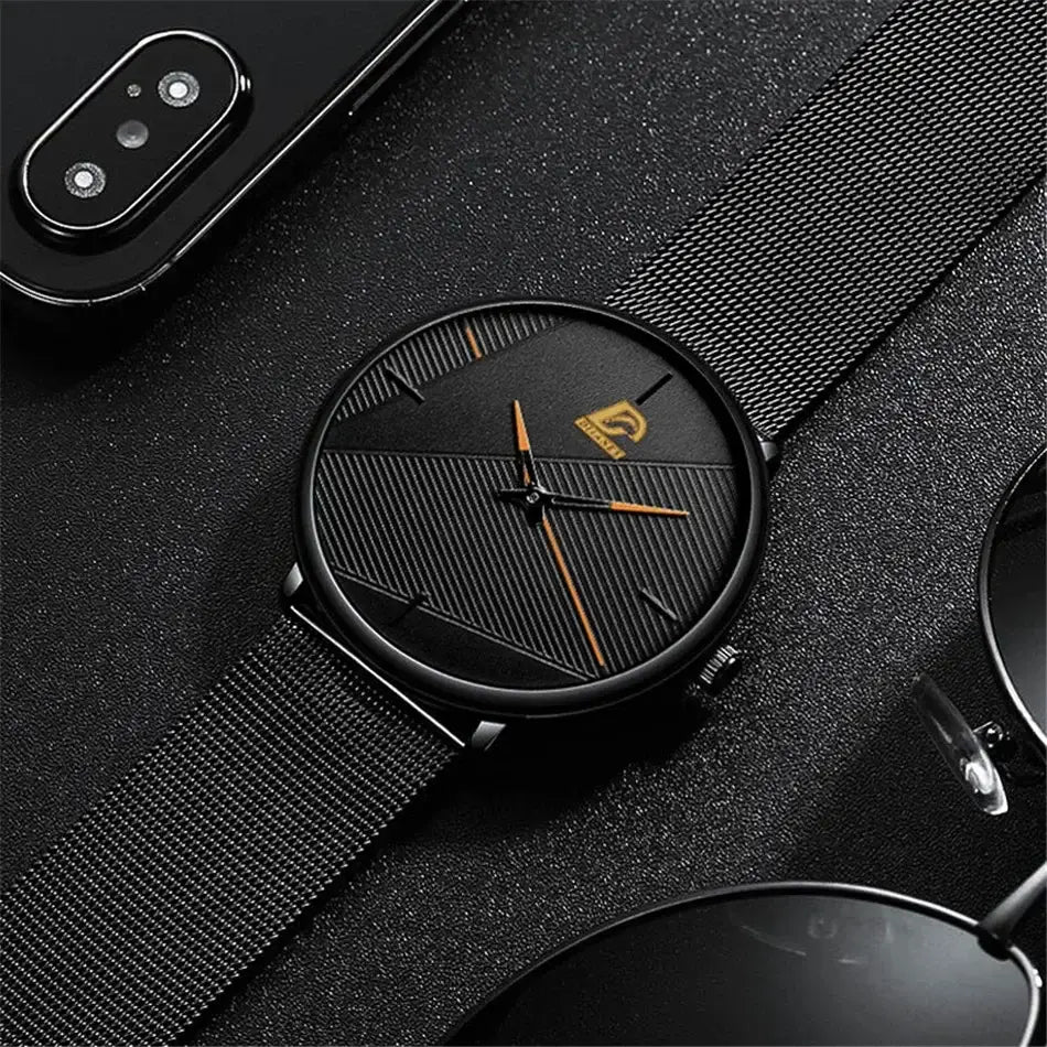 Herrenarmbanduhr aus schwarzem Mesh, Quarz, mit einem eleganten schwarzen Zifferblatt: dezente diagonale Linien, goldfarbene Zeiger und ein Markenlogo bei 12 Uhr.