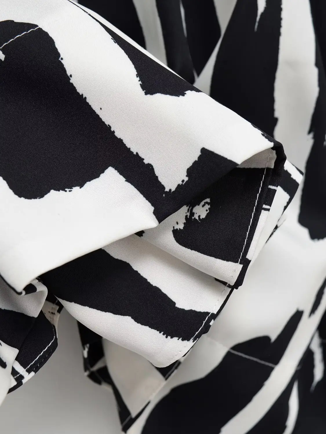 Ein schwarz-weißer abstrakter Pinselstrich-ge­musterter geometrischer Satin-Midirock mit weicher, fließender Textur