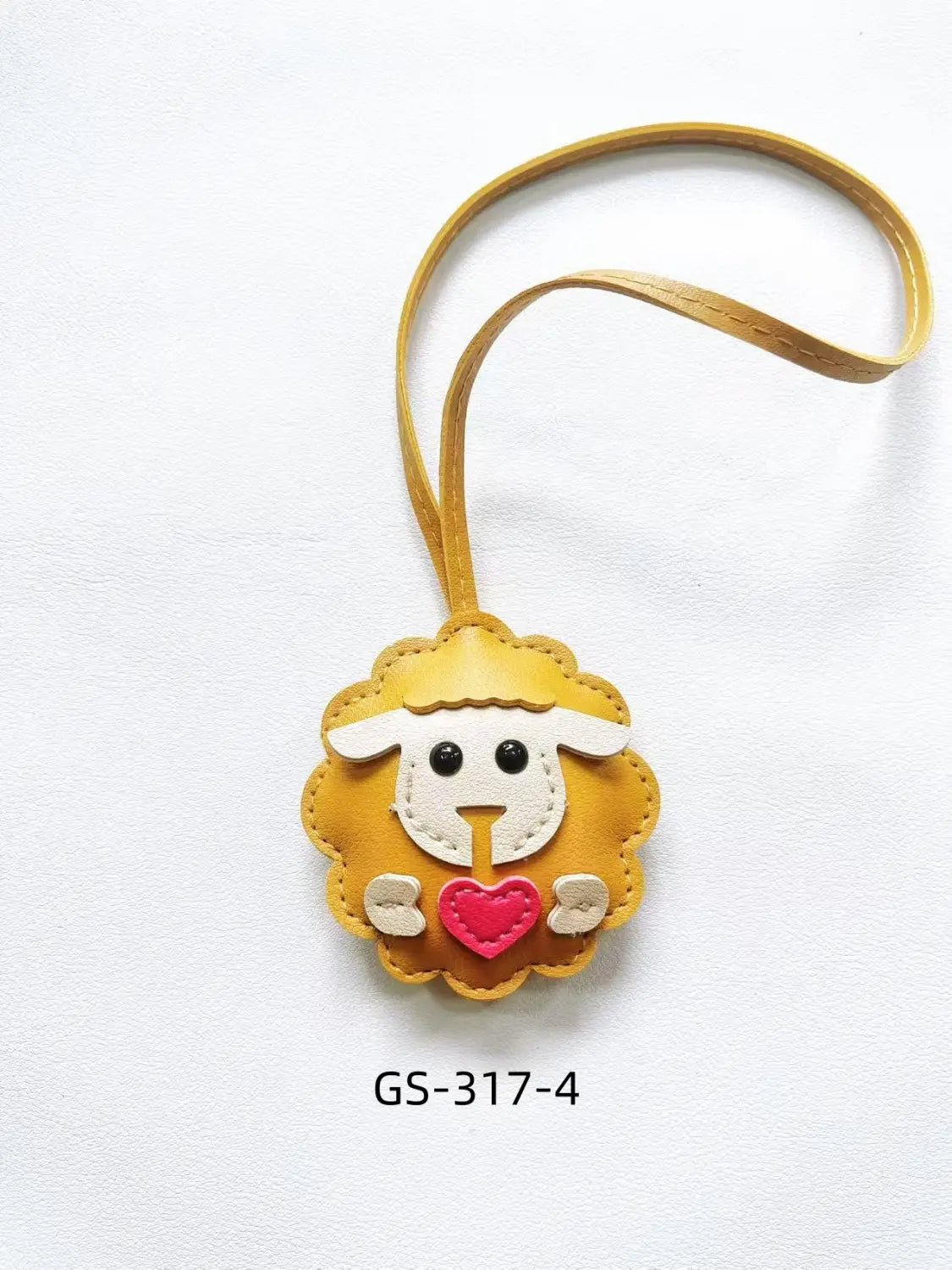 A charming mustard-yellow leather sheep keychain with a white face black eyes and a pink heart held in its paws used as a cute animal bag charm.