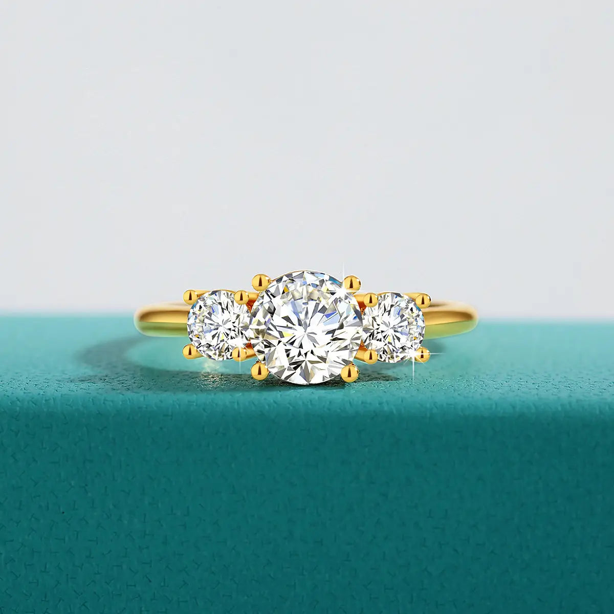 Bague trois pierres en moissanite en or 18 carats, avec une monture en or jaune, une pierre centrale taillée à facettes rondes brillant, flanquée de deux pierres plus petites assorties.