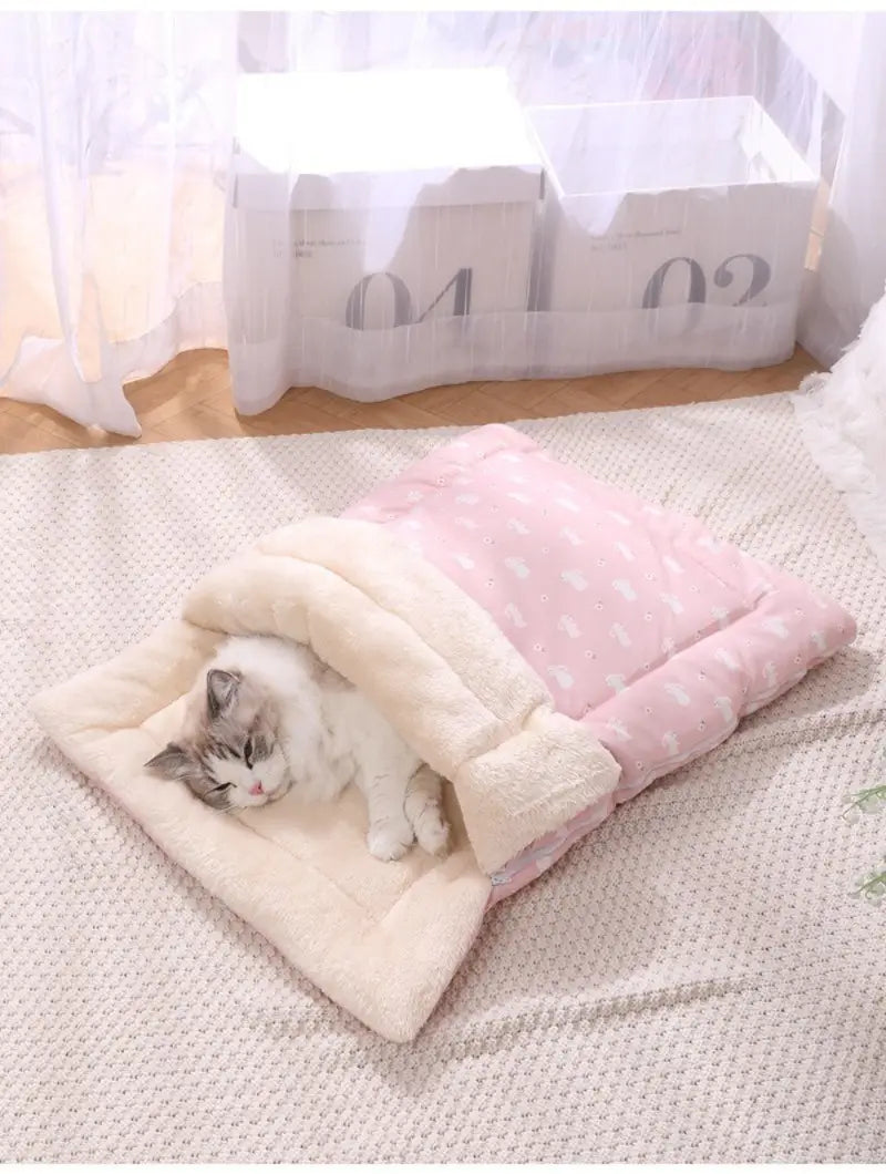 Cama acolchada para gato rosa y crema, diseñada como una bolsa de dormir suave y acogedora con forma de conejito, para brindar comodidad y descanso a su mascota