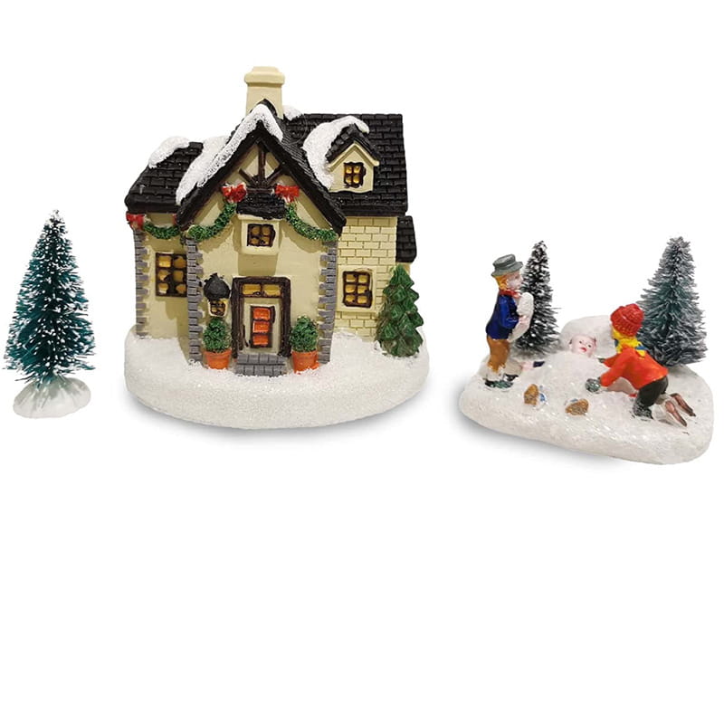 Weihnachtliches Dorf-Figürchen „Kinder spielen mit Schnee“: mit einem beigen Miniaturhaus mit schwarzem Schindeldach, das mit Schnee bedeckt ist, sowie mit festlicher grüner Girlande und roten Schleifen verziert.