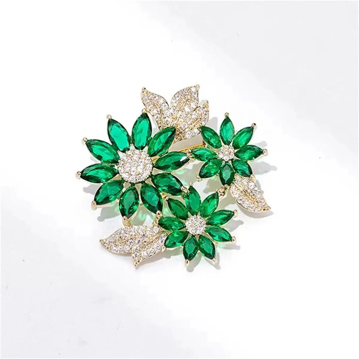 A sparkling green and white floral brooch pin featuring emerald-cut gemstones and pave-set diamonds on a gold-tone base.