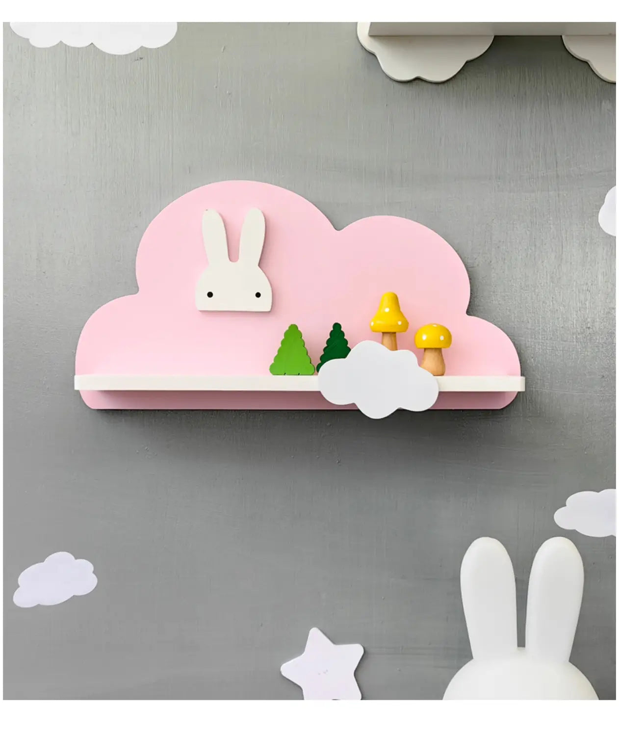 Das Regenbogen-Wolken-Bücherregal aus Holz für Kinder an der Wand verfügt über eine rosa, wolkenförmige Holzablage mit einem weißen Hasengesicht, grünen Bäumen und gelben Pilzen auf seiner Oberfläche.