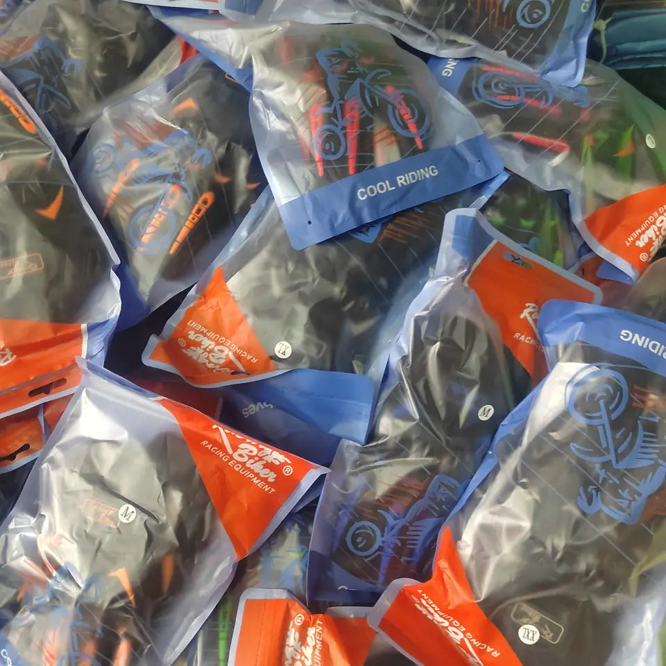 Black and orange motorcycle racing gloves with breathable protective gear visible through clear plastic packaging with blue branding.