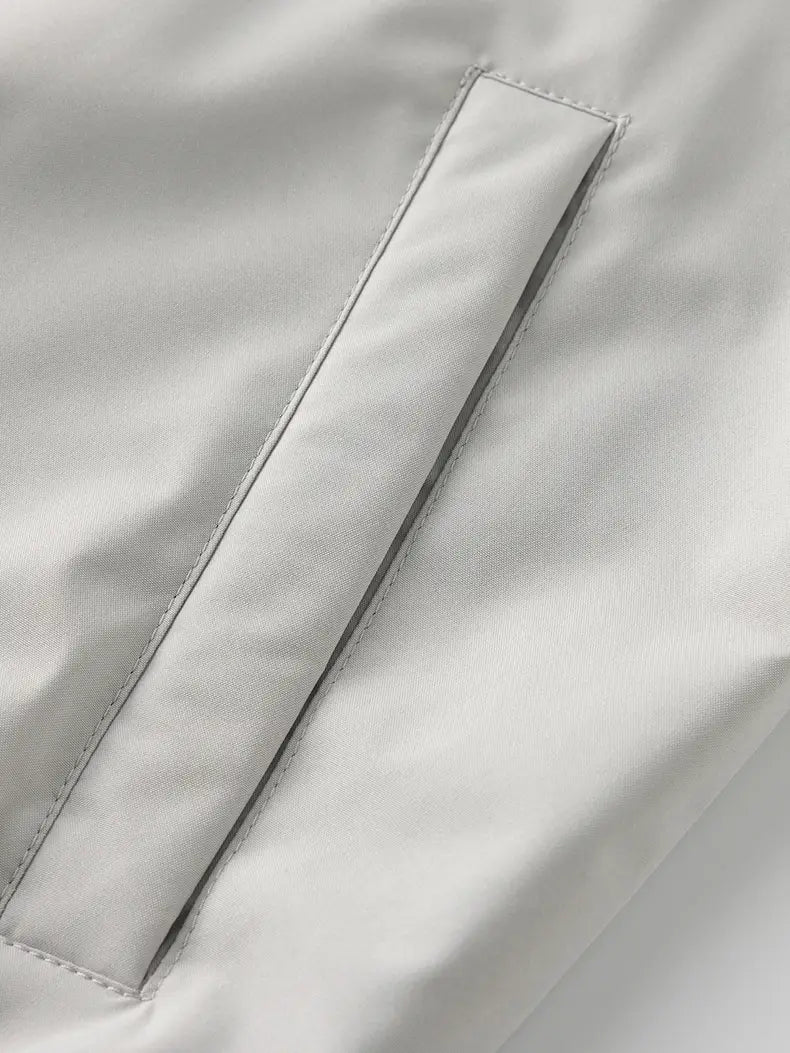 a sleek light gray fabric pocket with precise stitching and subtle sheen on a windbreaker waterproof hiking jacket for men