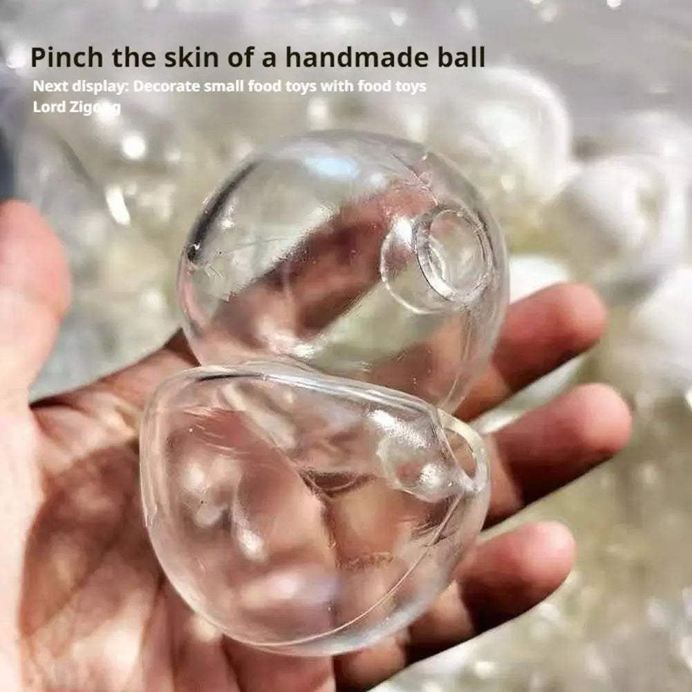 Jouet antistress sensoriel fait main en forme de balle molle, fabriqué en silicone translucide transparent, présentant une surface lisse légèrement texturée et de petites indentations circulaires.