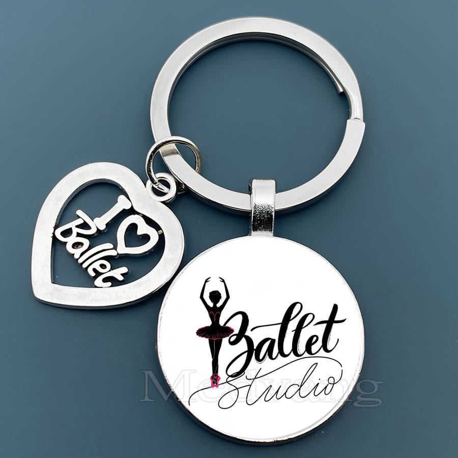 銀色のバレエをテーマにしたキーチェーンで、ハート形のチャームに「I heart ballet」の文字が入り、ガラスドーム内にバレリーナのシルエットと「ballet studio」の文字が描かれた円形ディスクをあしらったダンサーギフトデザイン。