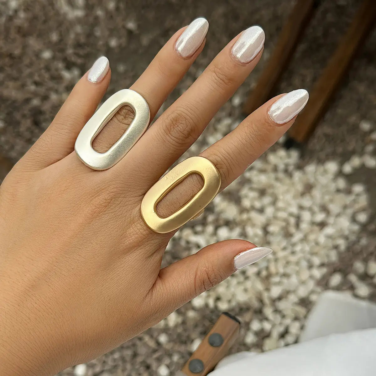 A hand wearing two bold geometric oval open rings for women with hollow center designs in silver and gold.