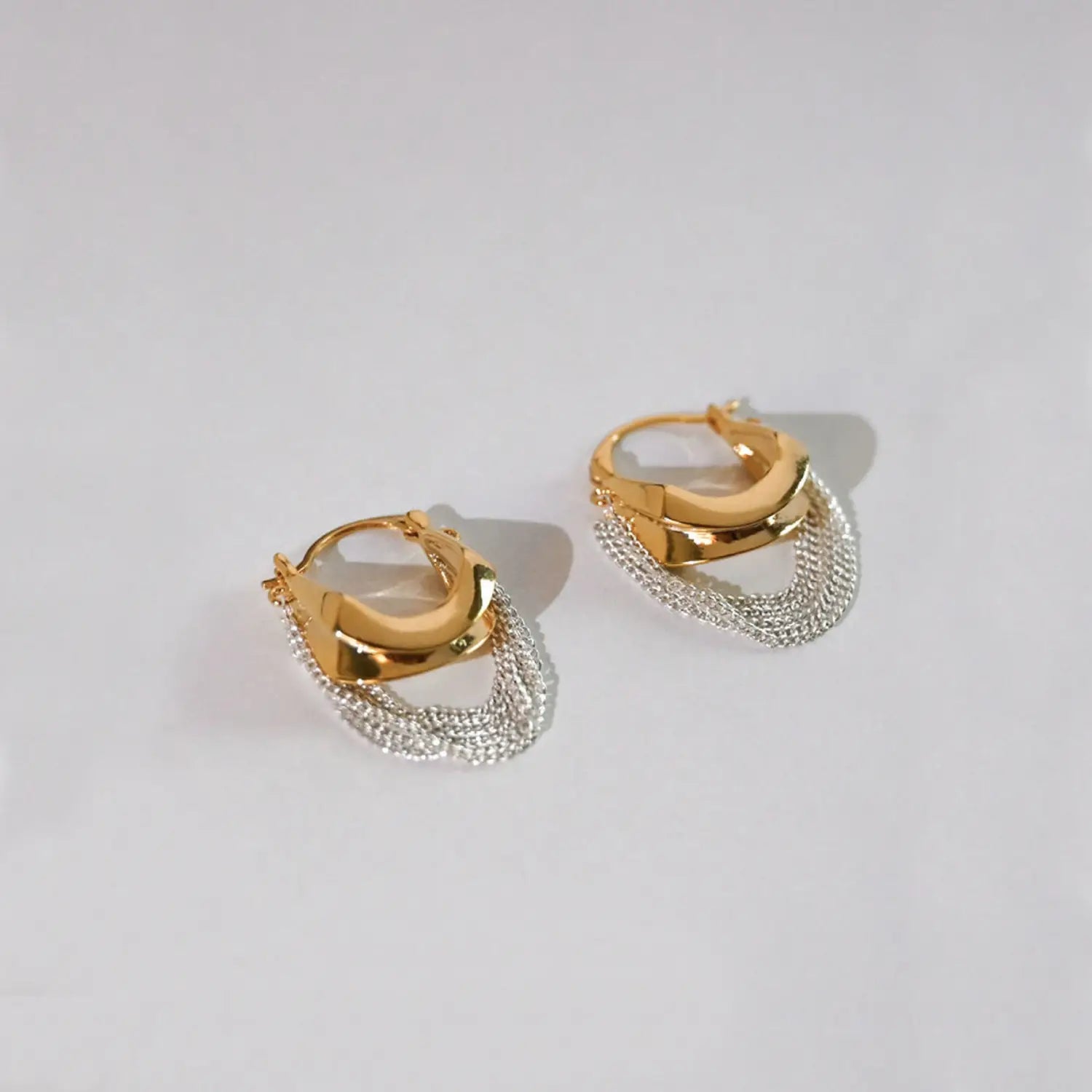 Goldfarbene Creolenohrringe mit modernem geometrischem Design und herabhängendem silbernem Kettenfransen-Detail, genannt Kettenquasten-Ohrhänger gold silber zweifarbig.