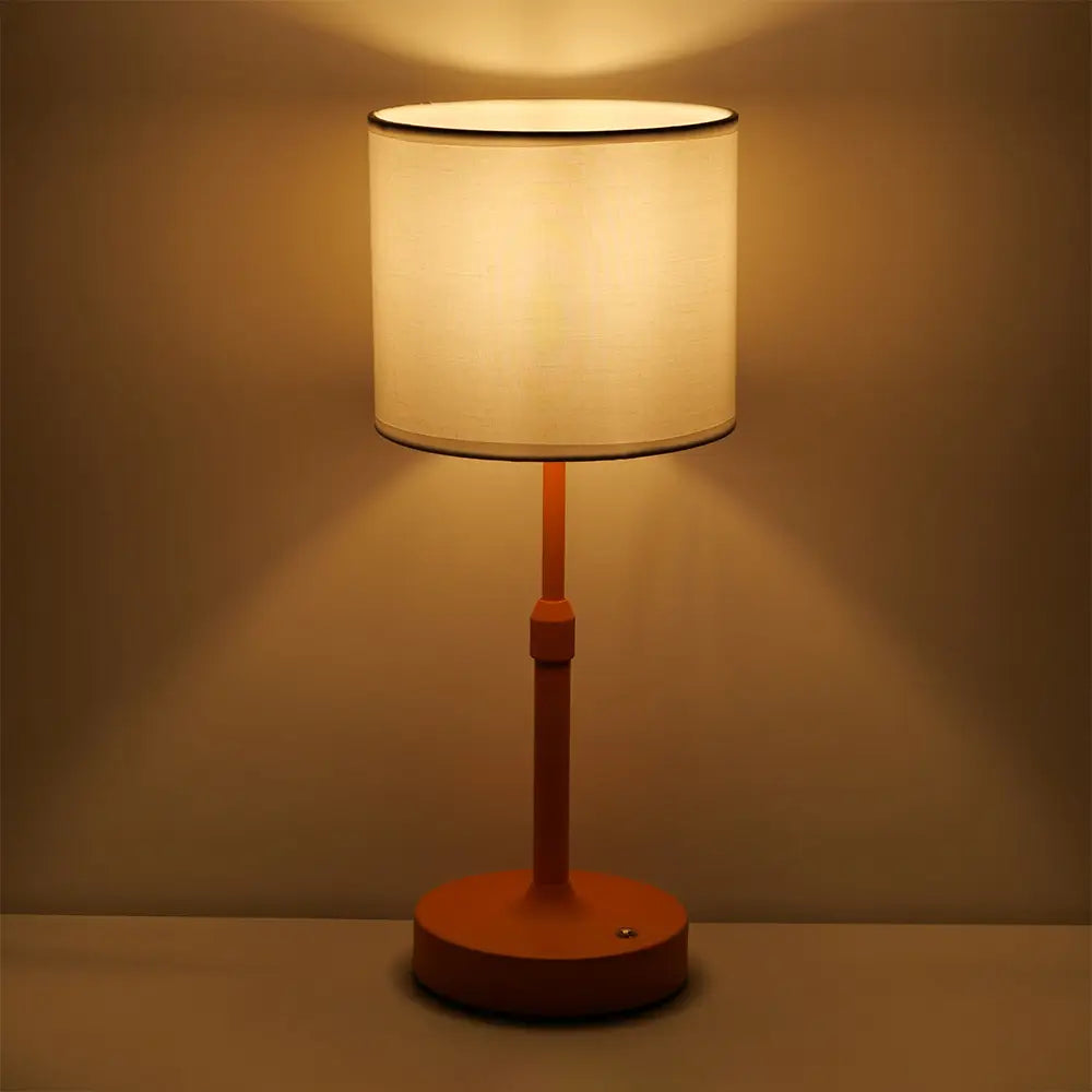 Plissierte Messing-Touch-Tischlampe mit einer warm orangefarbenen Metallbasis und einem weichen beigen zylindrischen Stoffschirm, von vorn dargestellt.