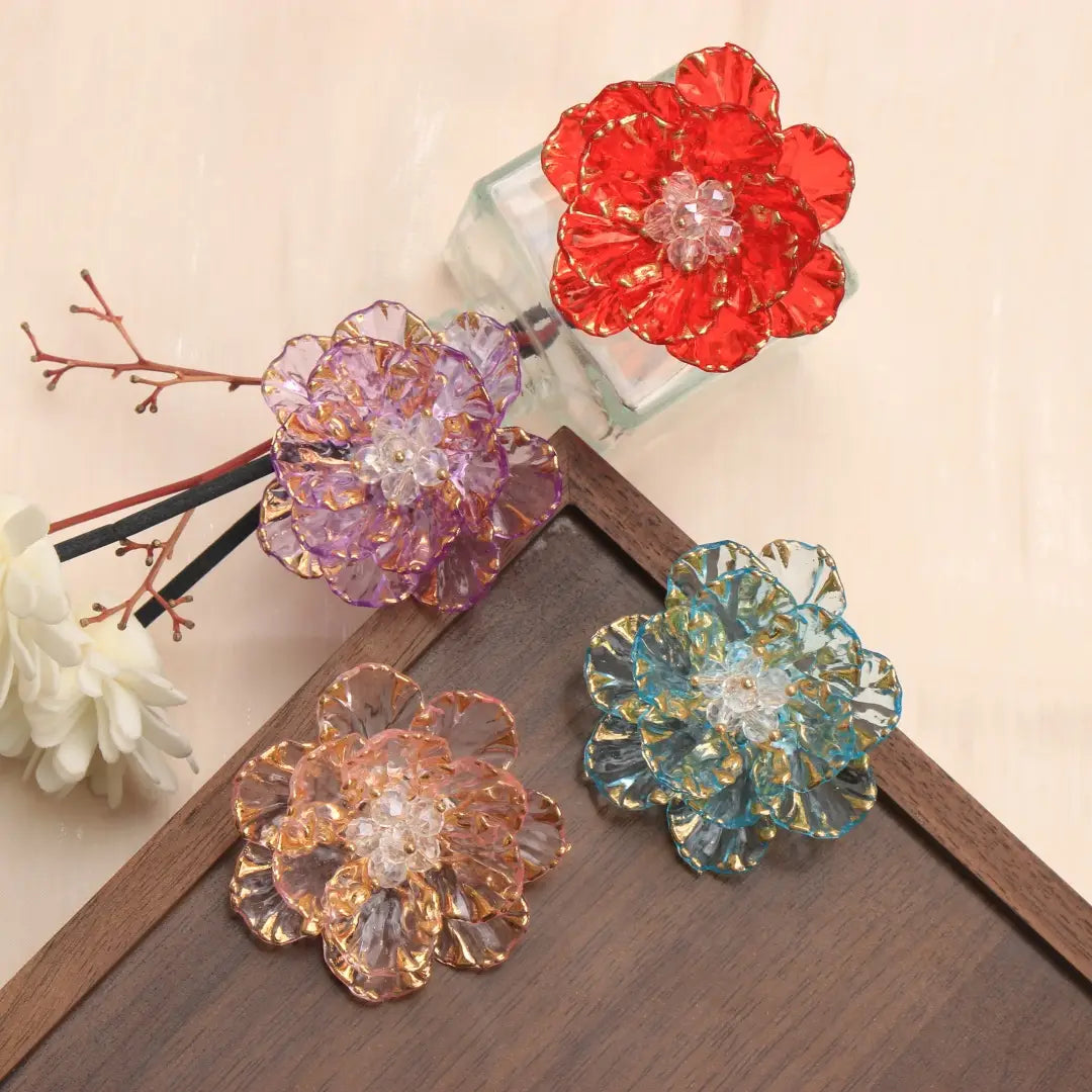 Broche en forme de fleur de cristal, accessoire de mode, présentant des barrettes pour cheveux en verre translucide aux couleurs vibrantes de fleur, en teintes rouge, pourpre, bleue et pêche, avec des pétales bordés d’or et des centres en cristal.
