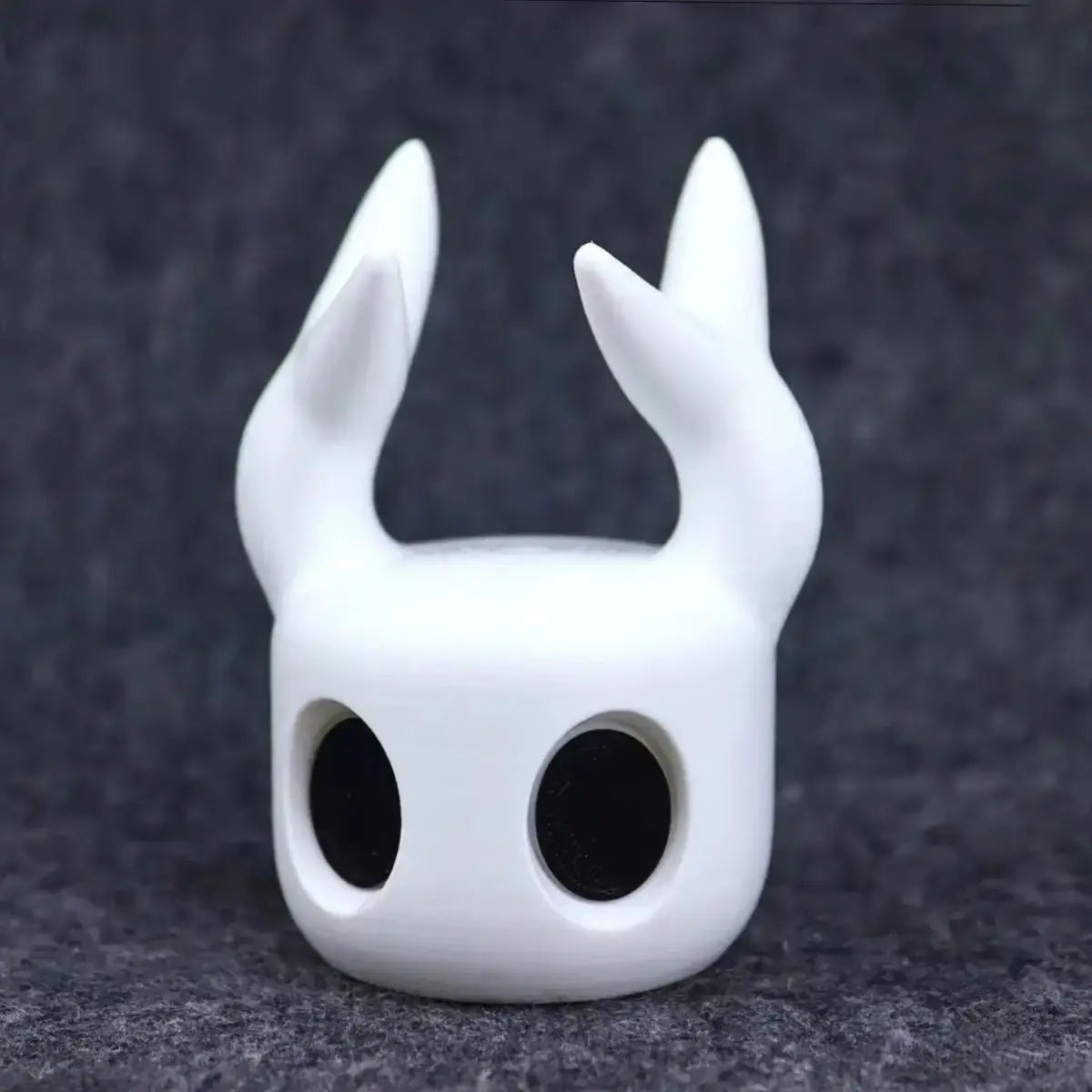 White smooth-surfaced Hollow Knight game controller stand for PS5 shaped like a stylized creature with two pointed ears and large black eye holes.